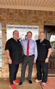 Three professionals smile in front of dental office